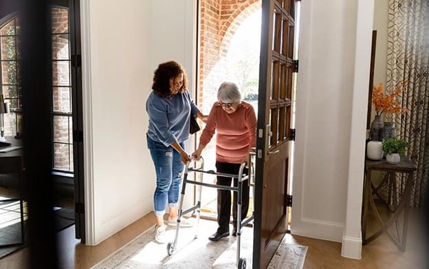 caregiver helping a senior woman with a walker