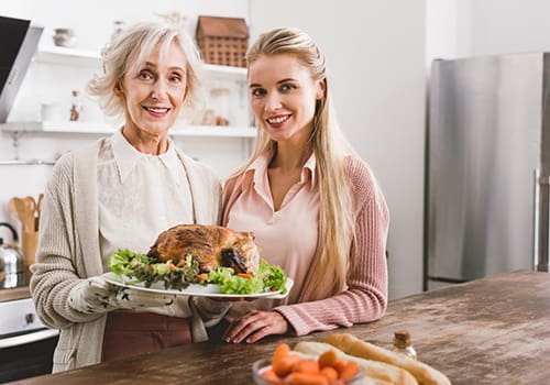 smiling mother and daughter holding plate with tasty turkey in Thanksgiving day