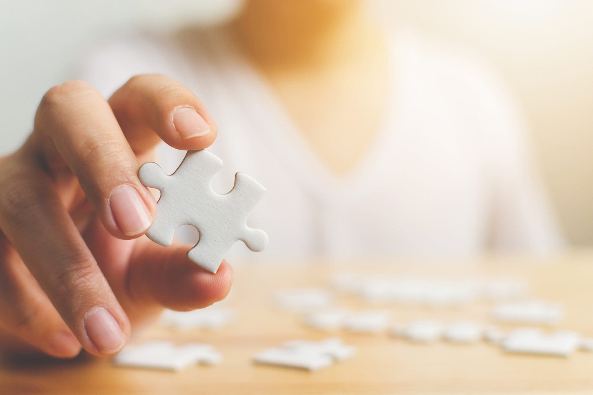 Hand of male trying to connect pieces of white jigsaw puzzle on wooden table. Healthcare for Alzheimer disease, dementia, memory loss, autism awareness and mental health concept