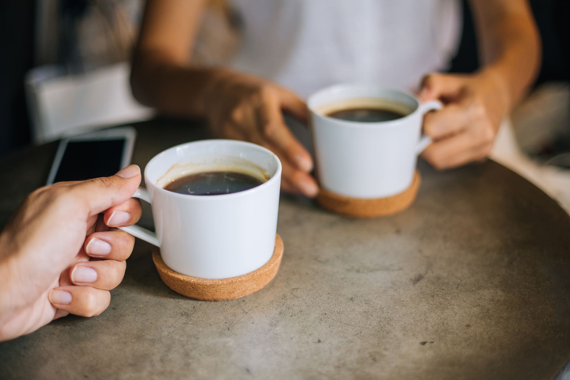 Close up woman and man holding cups of coffee on table