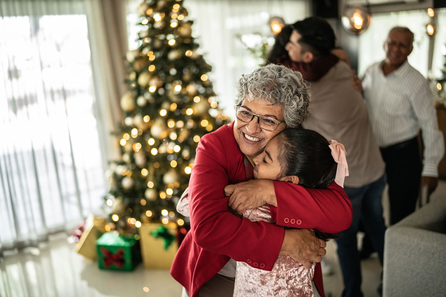 senior woman hugging her granddaughter in from of the christmas tree