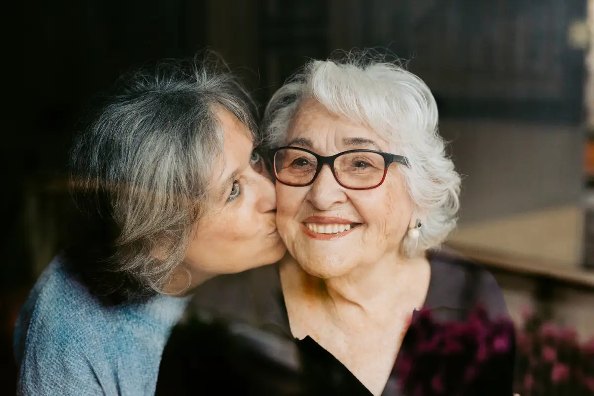 adult daughter giving her senior mother a kiss on the cheek